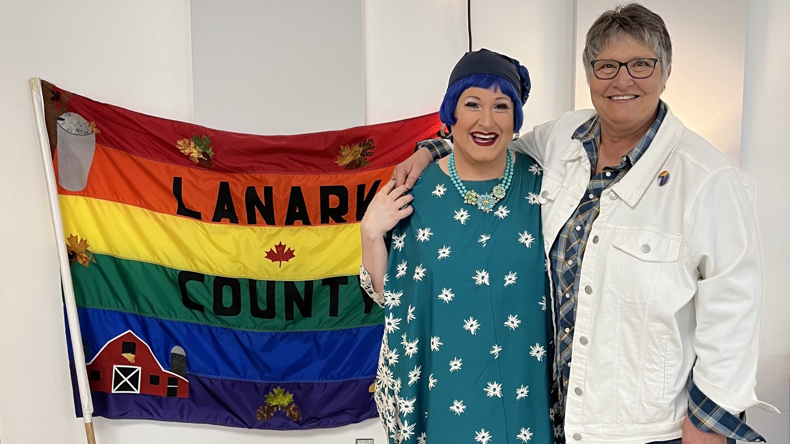 Tyffanie with Elizabeth of Queer Connection Lanark in front of thier Lanark County pride flag.